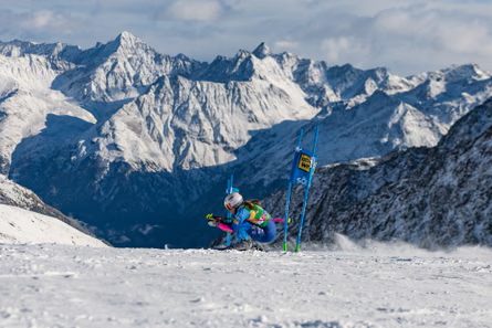 Paula Moltzan crouches low past a gate marker during a giant slalom run, mountains behind