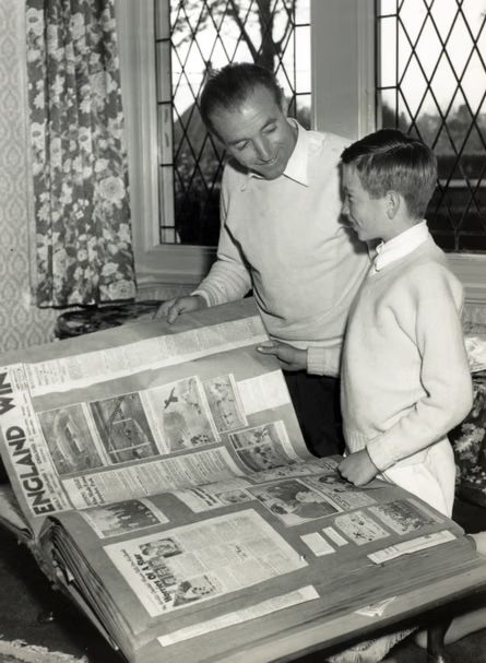 Footballer Stanley Matthews and his son smile looking at his football scrapbook