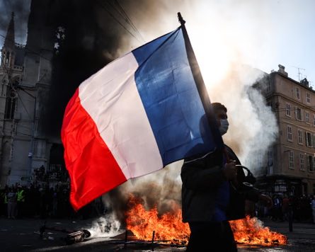 A protester waves a French national flag in front of a fire in the street