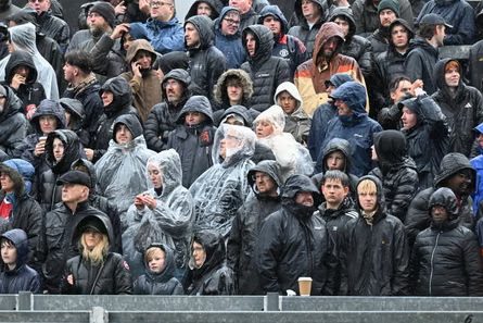 Swindon fans in hooded coats and clear plastic ponchos stand together in the rain