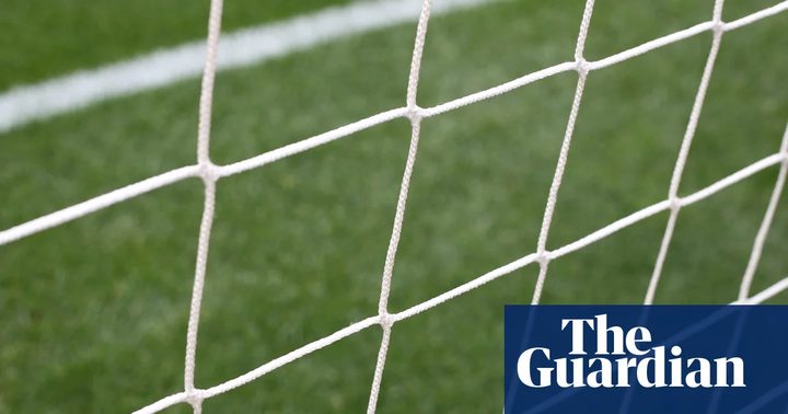 Un nen petit jugant a futbol en un camp mentre la gent l'observa.