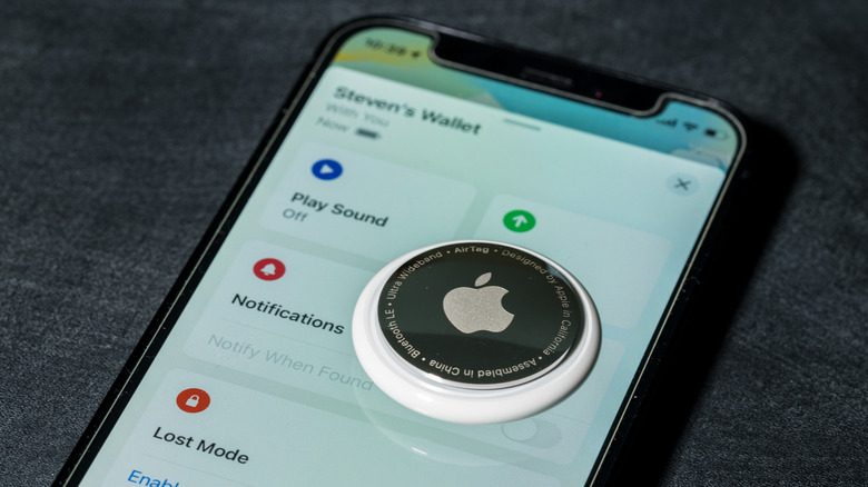 An Apple AirTag with its back cover facing up, sitting on top of an iPhone with the Find My app open.