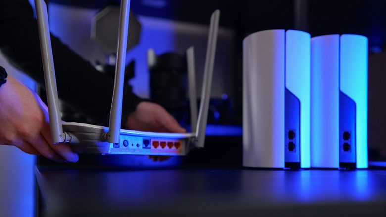Person setting up a router and mesh network in a dark, blue neon-lit room.