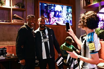 Shola Ameobi smiles alongside a fan while a photo is taken on a phone