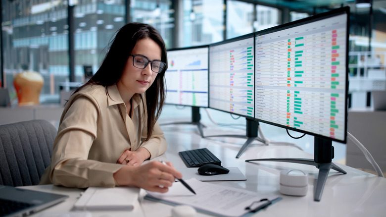 A woman working in an office with spreadsheets on the monitors.