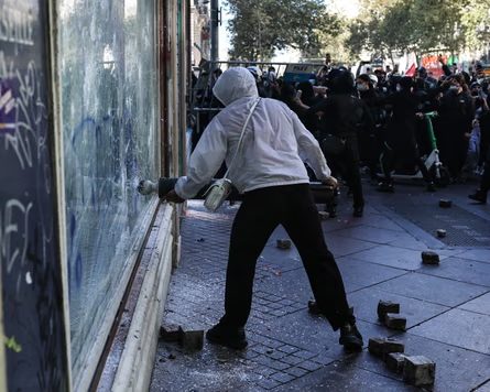 A protester in a white hoodie smashes a window during a Marseille demonstration