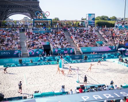 People playing beach volleyball on a sandy beach volleyball court with stands all around it