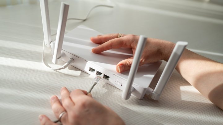 Un rúter Wi-Fi modern situat en un prestatge al costat d'aparells electrònics.