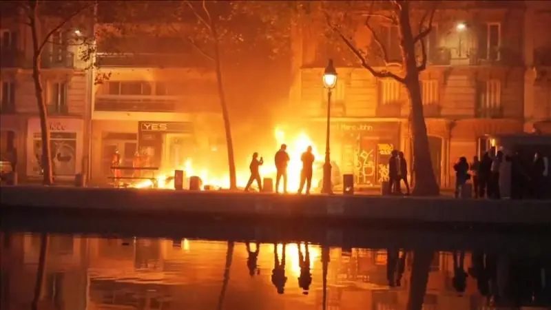 Personas en la calle en la noche y fuego delante de edificios.