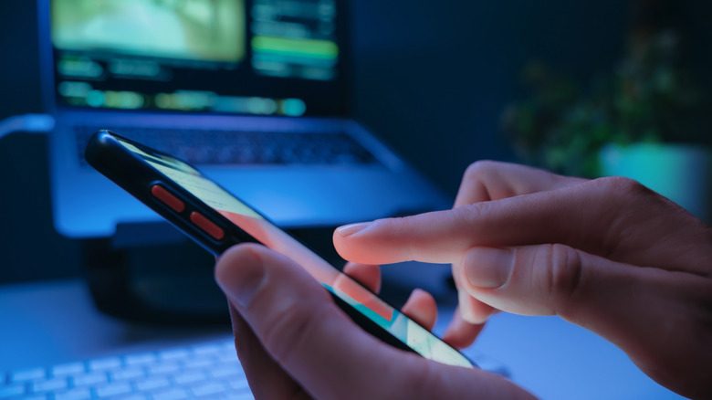 An unknown person uses a phone in front of their laptop