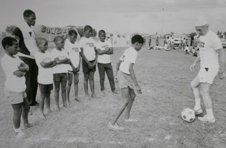 Stanley Matthews dribbles a football while a line of boys in Soweto club shirts watch