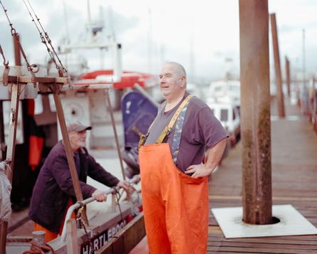 Fisherman Stan Rennie in orange waders stands on a harbour dock near fishing boats