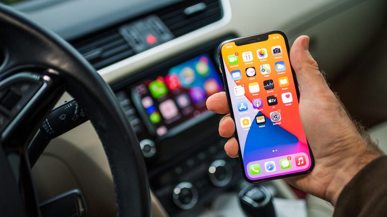 A person holding an iPhone in front of a car's infotainment system with CarPlay running.